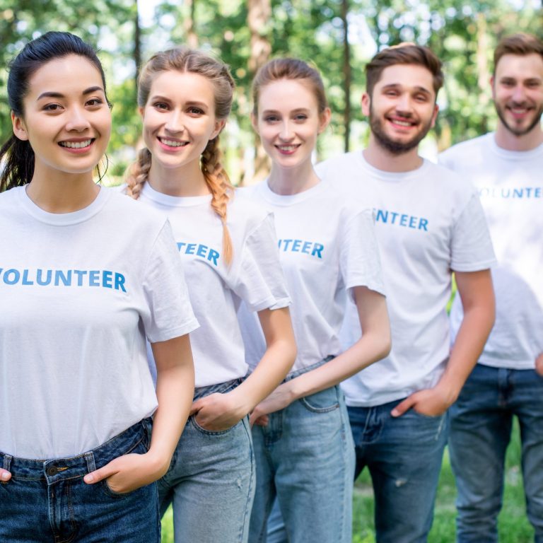 young smiling volunteers standing in row in park